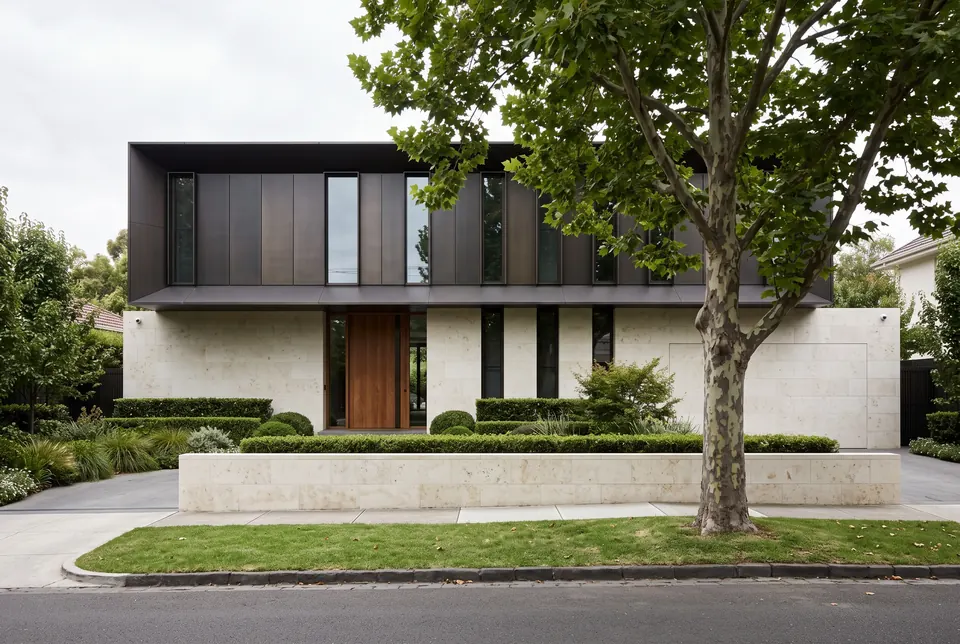 Two-storey Toorak residence in honed limestone and dark bronze behind a clipped hedge and a plane tree